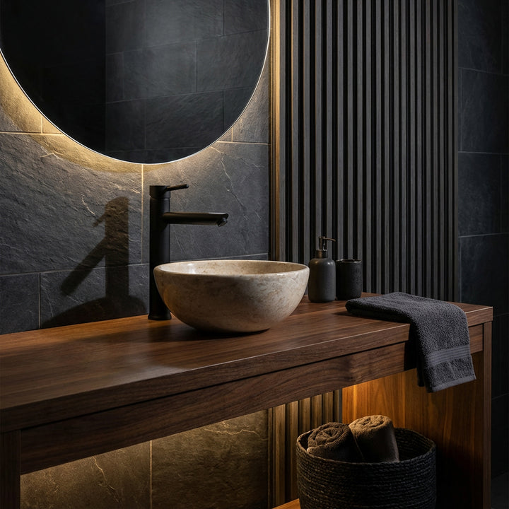 Vasque à poser ronde en pierre naturelle claire sur lavabo en bois foncé avec robinetterie noire dans une ambiance de salle de bain élégante