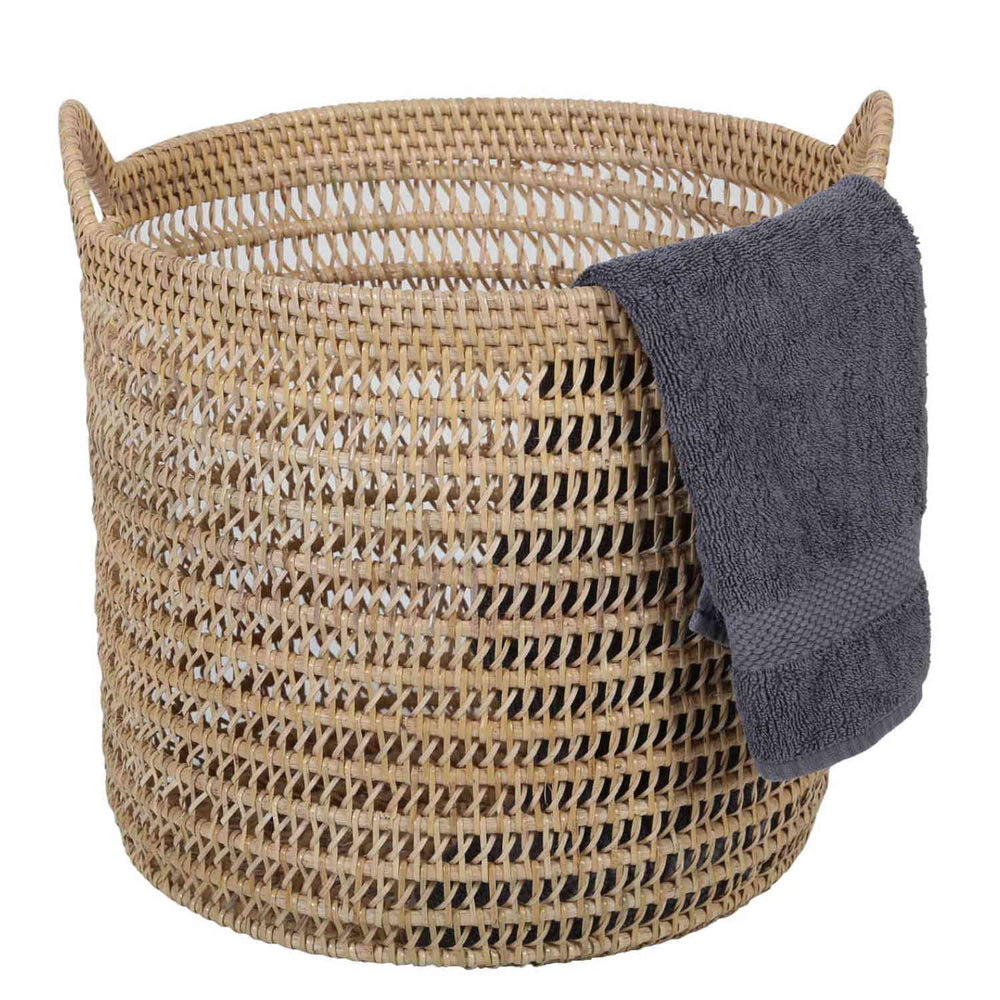 Panier Eda en rotin naturel, tressage ajouré, deux anses et serviette gris foncé posée sur le bord.