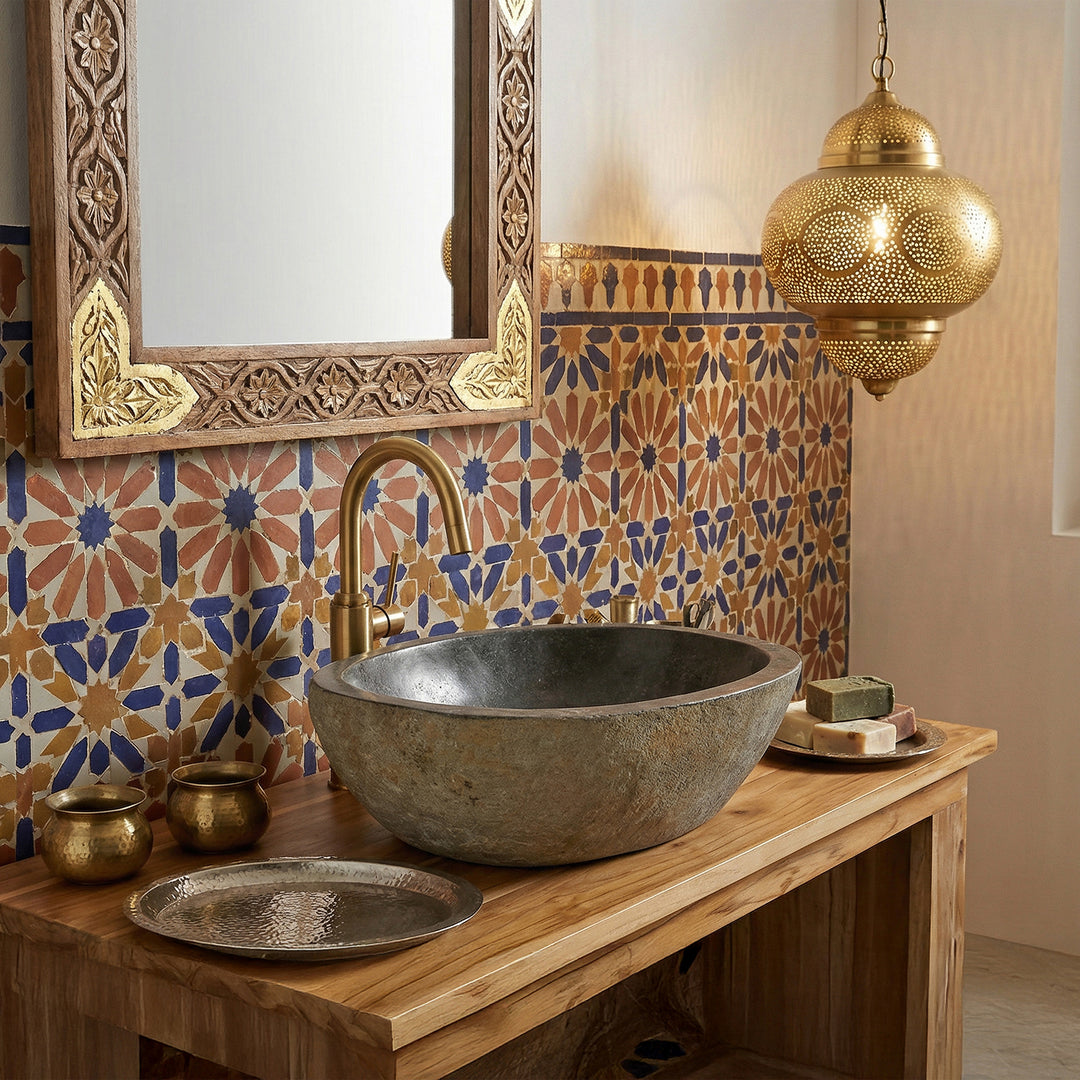 Pierre de rivière Lavabo dans la salle de bain orientale sur une console en bois, associée à des robinetteries en laiton, des carreaux de mosaïque et une lumière chaude