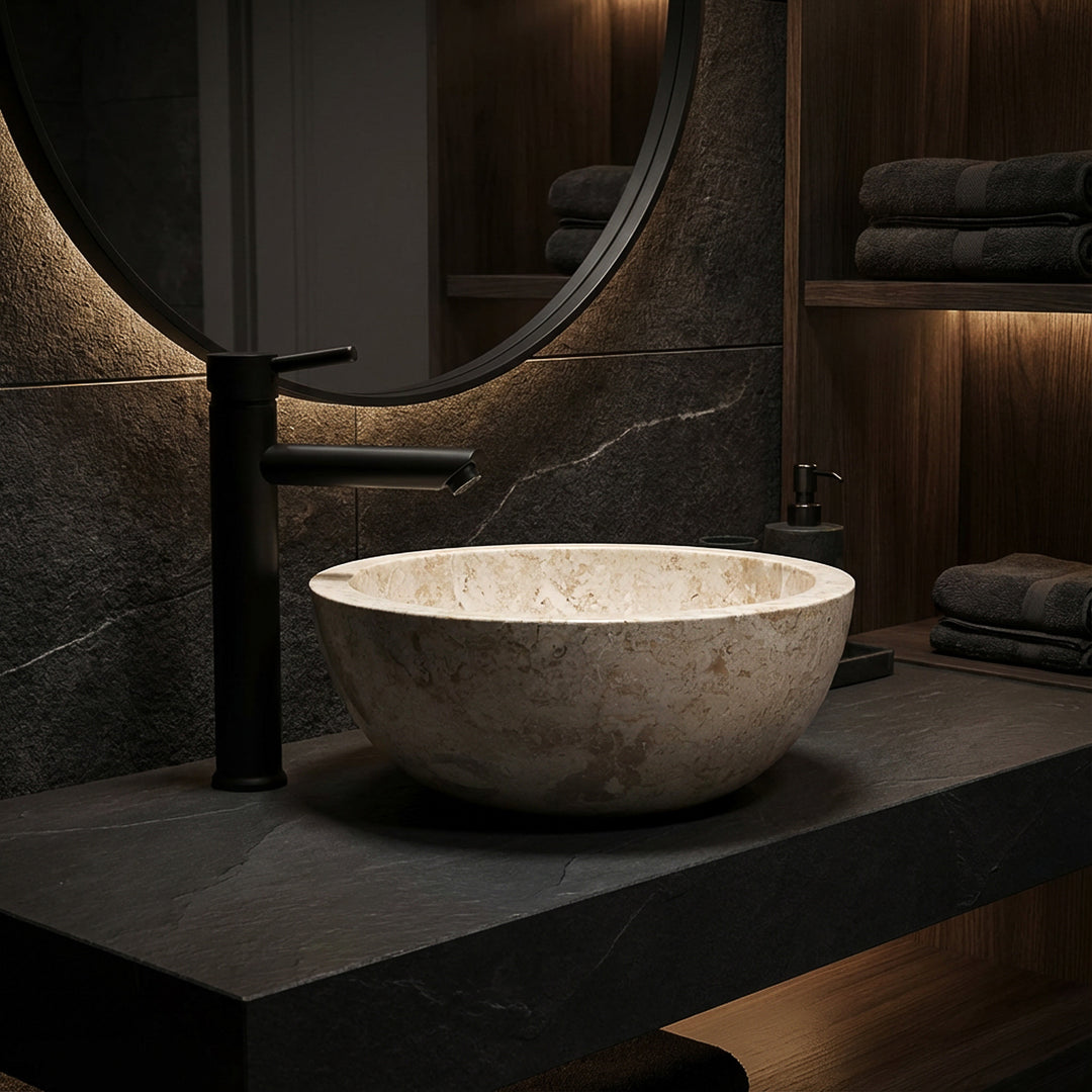 Vasque ronde à poser en marbre clair sur dalle de pierre foncée avec robinetterie noire dans une ambiance de salle de bain élégante