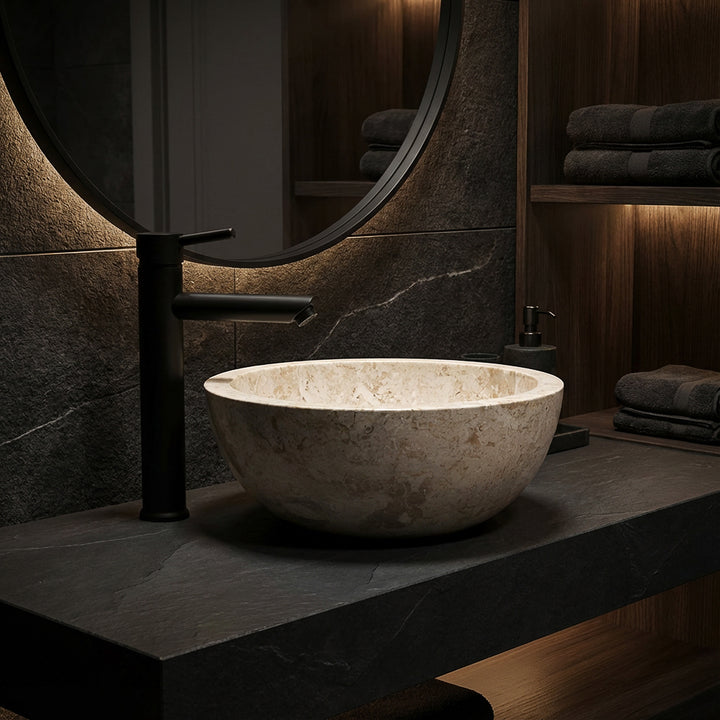Vasque ronde à poser en marbre clair sur dalle de pierre foncée avec robinetterie noire dans une ambiance de salle de bain élégante