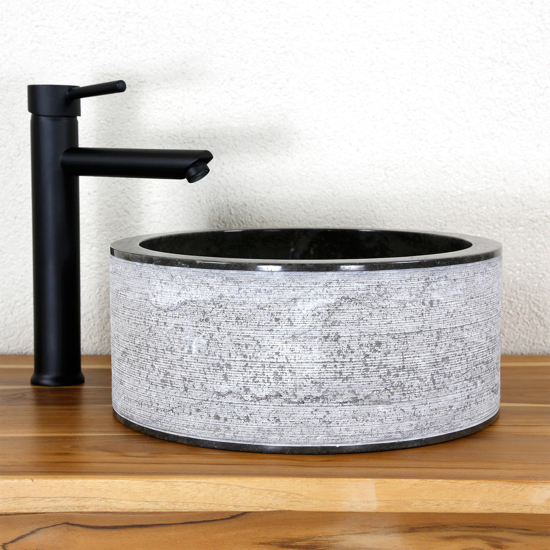 Lavabo à poser rond en pierre naturelle avec une structure aux lignes marquantes, associé à un robinet sur pied noir sur bois.
