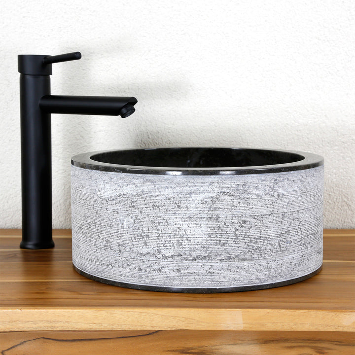 Lavabo à poser rond en pierre naturelle avec une structure aux lignes marquantes, associé à un robinet sur pied noir sur bois.
