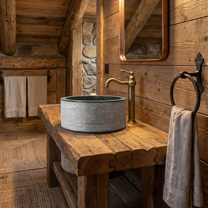 Lavabo à poser rond en pierre sur une table en bois massif, combiné à des raccords en laiton dans une salle de bain de chalet rustique.