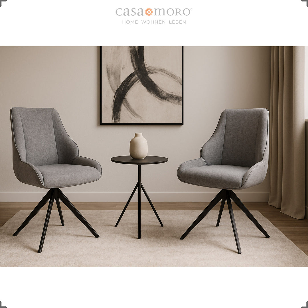 Zwei 360° drehbare Esszimmerstühle in Grau mit schwarzem Metallgestell neben rundem Beistelltisch in modernem, hell eingerichteten Wohnraum