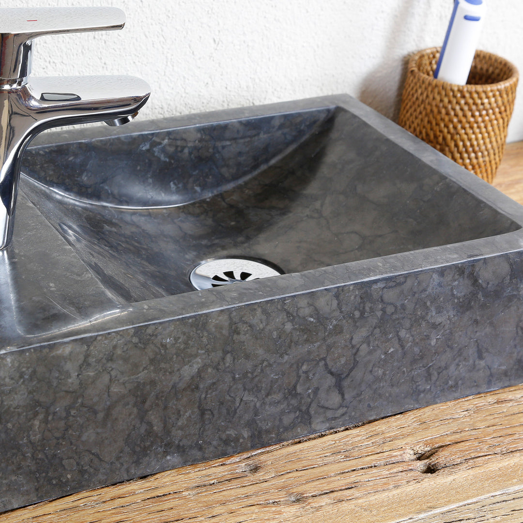 Vasque à poser angulaire en pierre naturelle à grain foncé en vue détaillée, avec vidage en acier inoxydable et raccord chromé sur plaque de bois