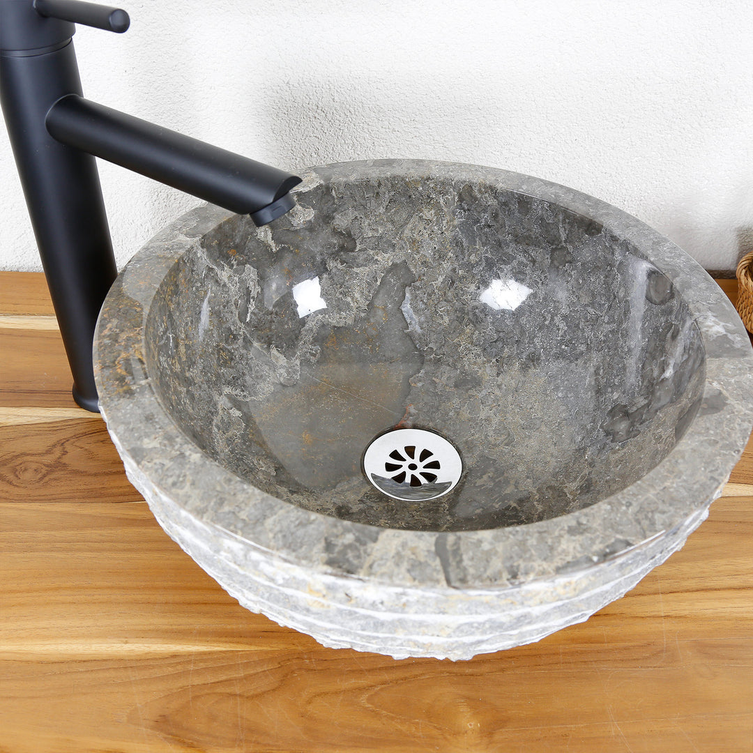 Vasque à poser ronde en pierre naturelle avec surface intérieure polie et bord extérieur structuré sur un plateau en bois