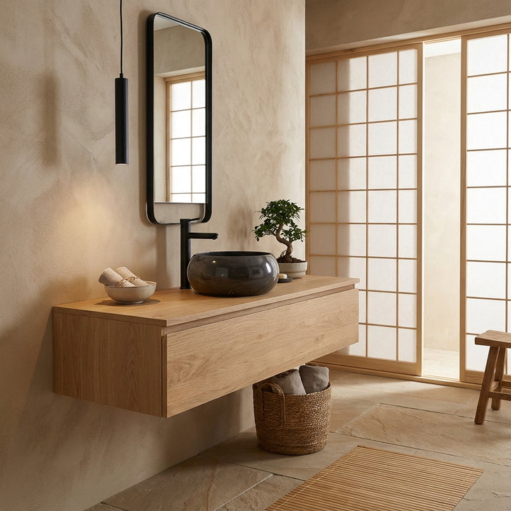 Lavabo rond en pierre sur meuble sous-vasque flottant en bois dans une salle de bains d'inspiration japonaise, combiné avec des raccords noirs, un miroir à cadre en bois et une lumière naturelle douce