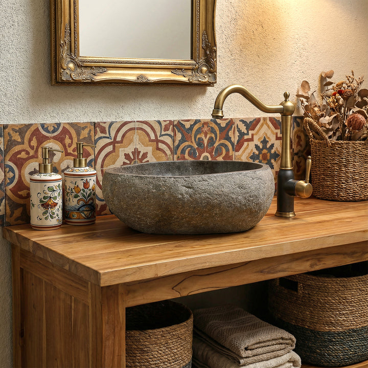 Lavabo en pierre naturelle dans une salle de bains bohème chaleureuse sur meuble sous-vasque en bois, combiné avec des raccords en laiton et des carreaux à motifs