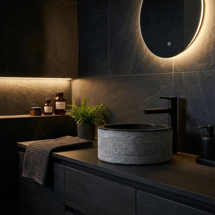 Lavabo rond en pierre avec une structure fine sur une console en bois sombre, mis en scène de manière atmosphérique dans la salle de bains moderne à l'ambiance sombre.