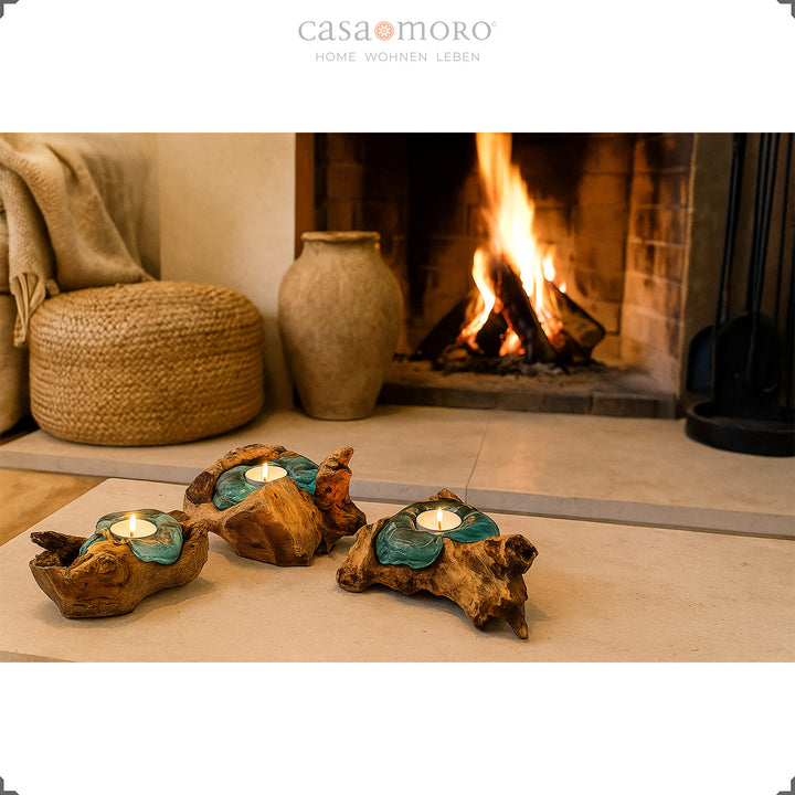 Drei Teelichthalter aus Glas und Wurzelholz vor einem brennenden Kamin, ihr sanftes Licht unterstreicht die gemütliche Wohnatmosphäre.