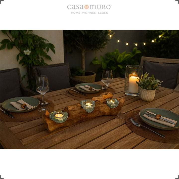 Dreiteiliger Teelichthalter aus Glas und Wurzelholz als stimmungsvolle Tischdeko auf einer Terrasse, eingerahmt von Pflanzen und gedecktem Tisch