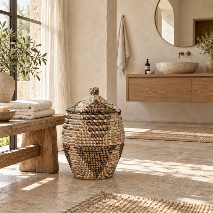 Panier bombé en jonc de mer à couvercle conique fermé, près d’un banc en bois et d’un meuble-vasque dans la salle de bains.