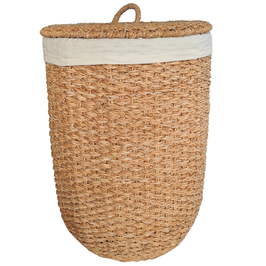 Panier à linge ouvert en jonc de mer de couleur naturelle, avec un empiècement en tissu clair et un couvercle reposant sur le côté.