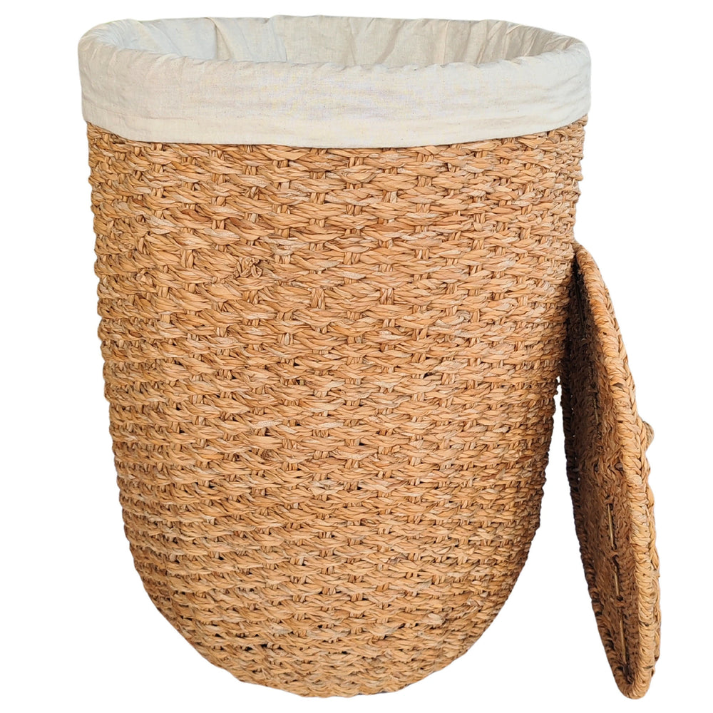Panier à linge ouvert en jonc de mer de couleur naturelle, avec un empiècement en tissu clair et un couvercle reposant sur le côté.