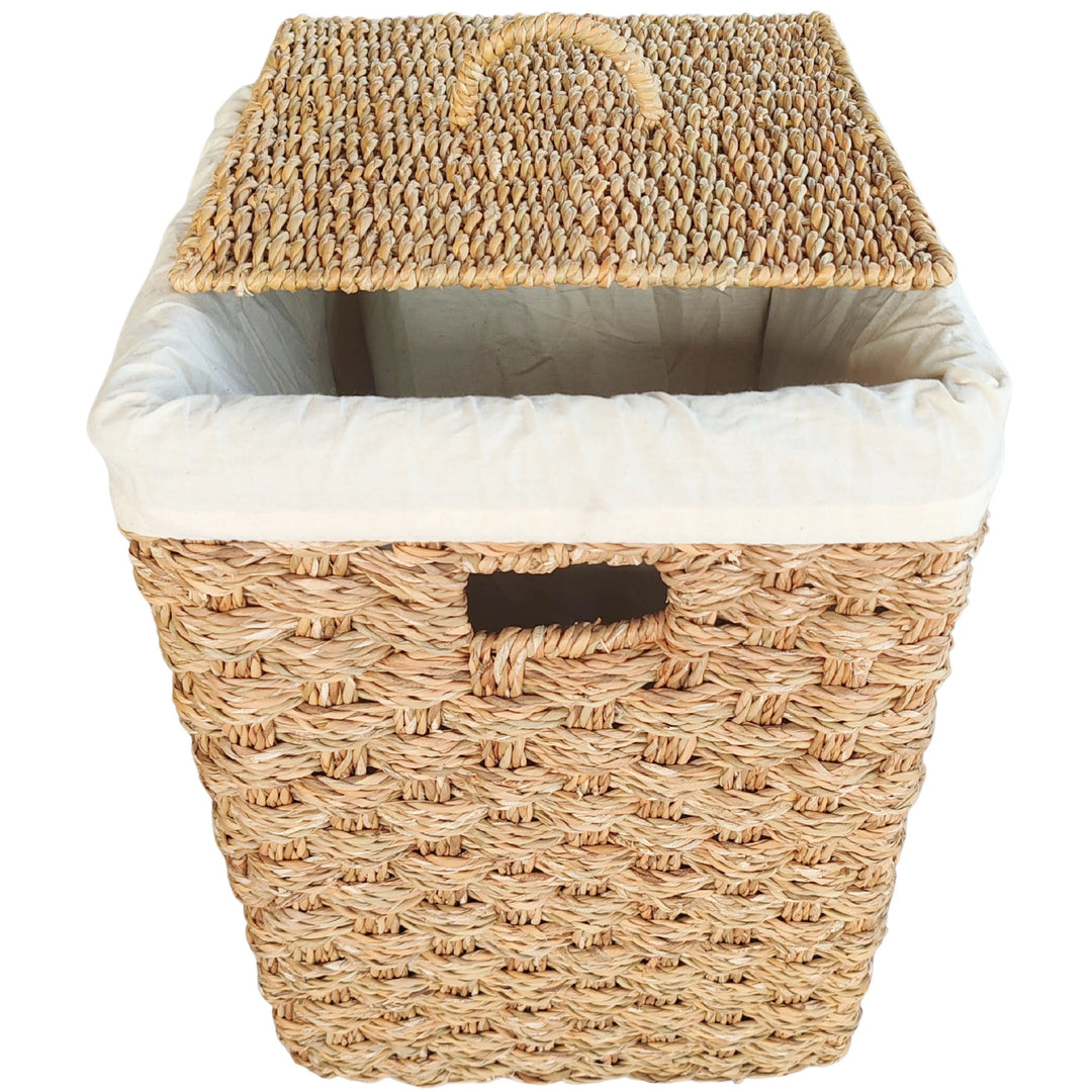 Panier à linge carré en jonc de mer, doté d'un couvercle surélevé, d'un insert en tissu clair et d'une poignée intégrée.