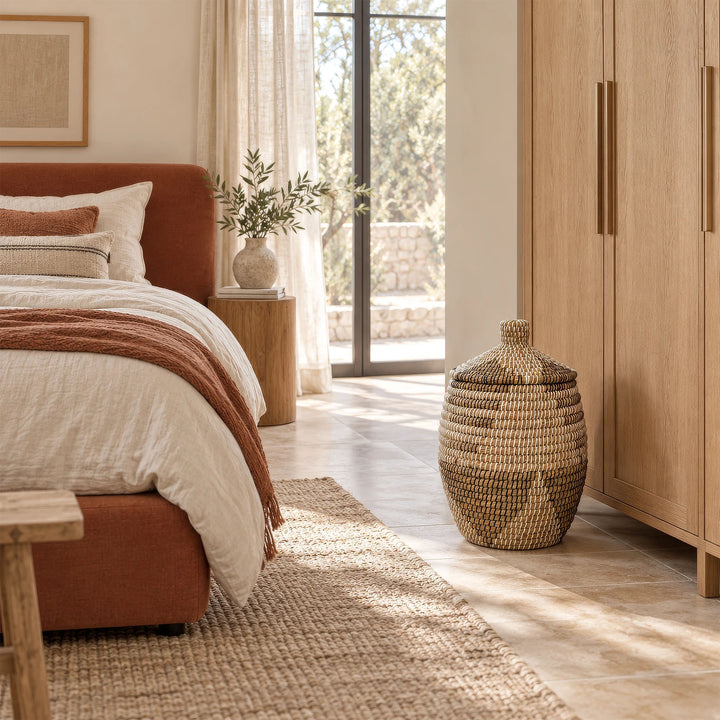 Panier brun naturel en jonc de mer, motifs blancs et noirs, couvercle conique fermé, devant une armoire en bois.