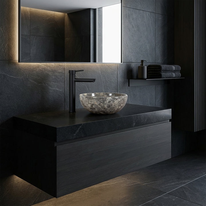 Lavabo rond à poser en pierre naturelle avec grain gris-brun sur un lavabo sombre dans la salle de bain moderne, combiné avec des raccords noirs et un design mural sombre