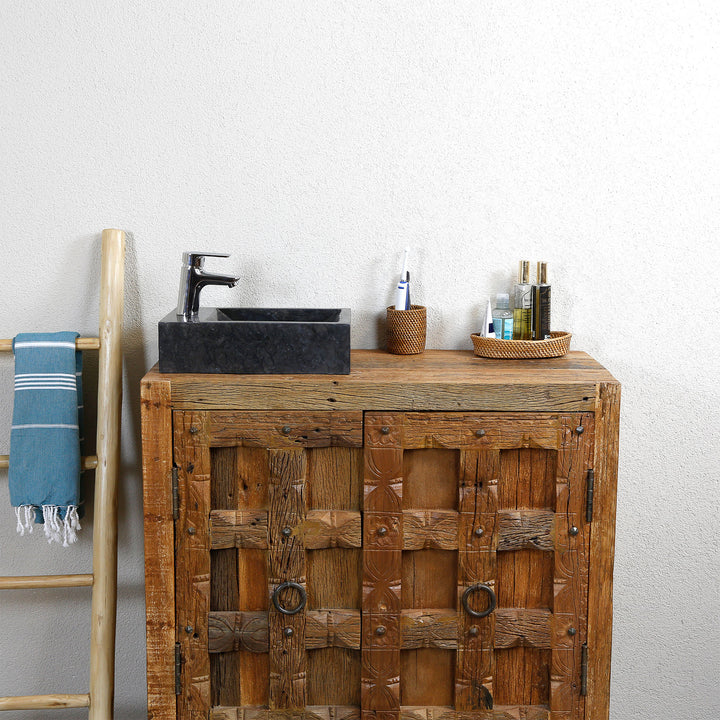 Lavabo carré à poser en marbre à grain foncé sur un lavabo en bois rustique, combiné avec des robinetteries chromées et des accessoires naturels devant un mur clair