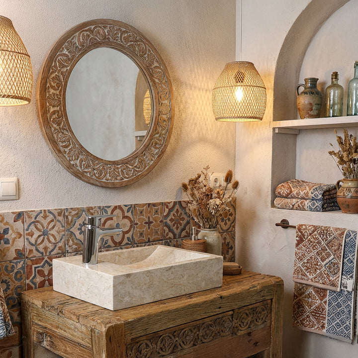 Lavabo rectangulaire à poser en pierre naturelle claire sur un lavabo en bois dans une salle de bains orientale avec carrelage à motifs et lumière chaude