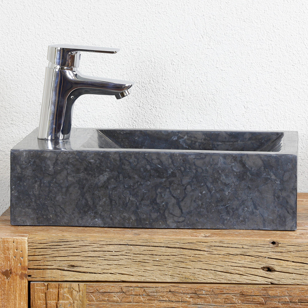 Vasque à poser carrée en marbre au grain foncé sur une console en bois, associée à des ferrures chromées devant un mur clair