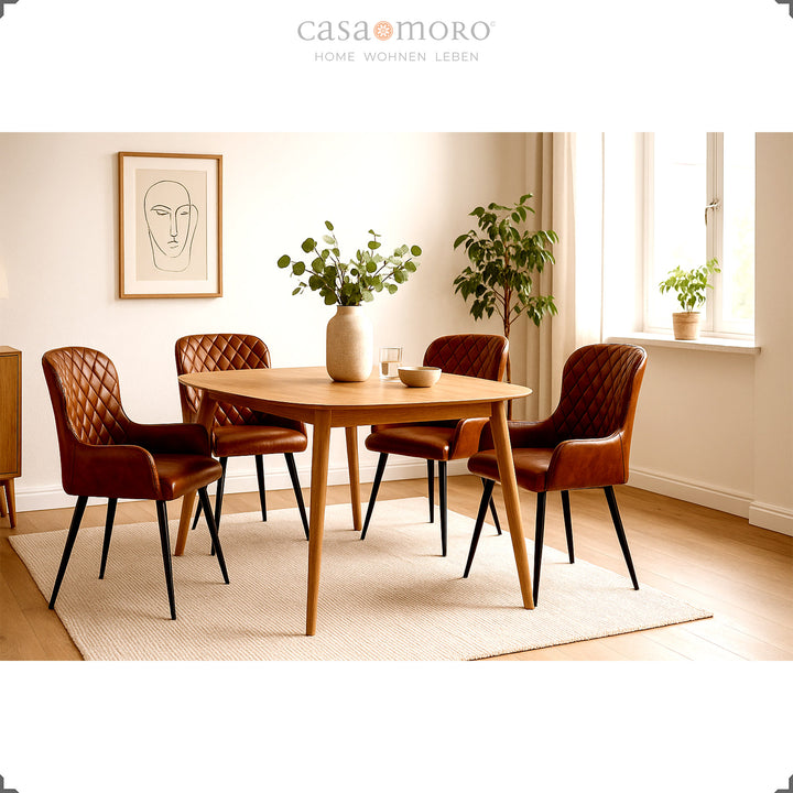 Vier antikbraune Lederstühle mit Rautensteppung um einen runden Holztisch in einem hellen, freundlich eingerichteten Wohnzimmer mit Pflanzen und Tageslicht.